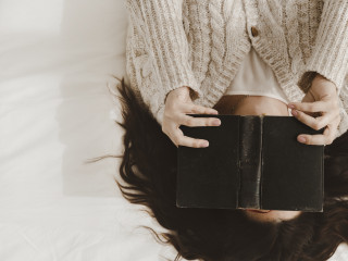 young woman covering face with book